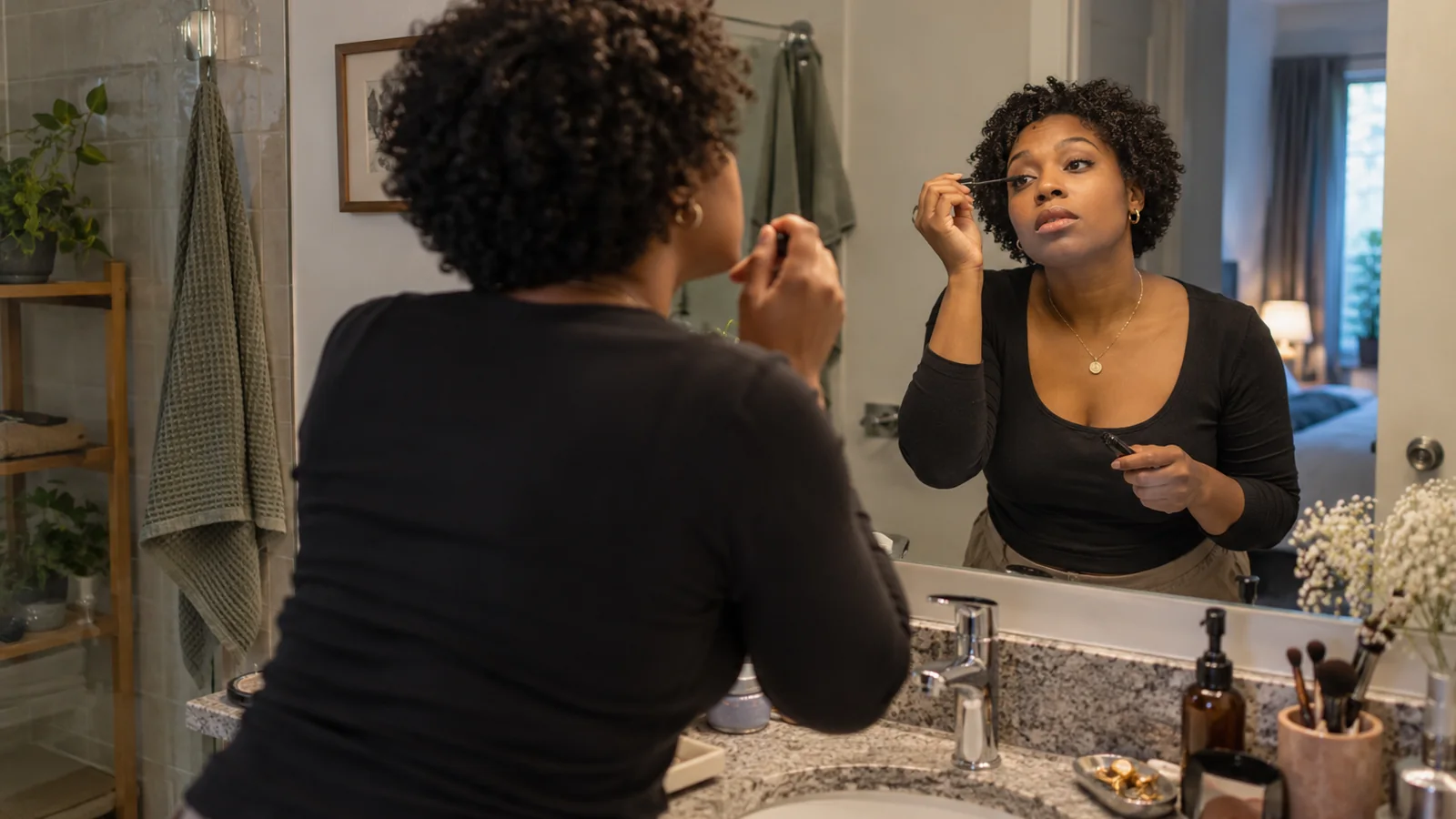 Black woman with natural curls applying simple makeup at her bathroom mirror before work